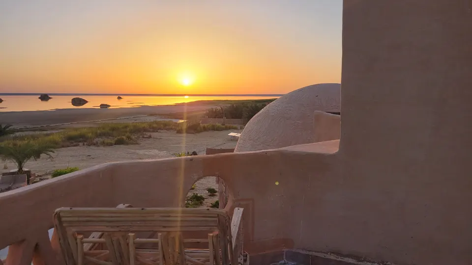 Sunrise over Siwa Salt Lake from a quiet terrace, with wooden chairs and the lodge’s curved domes
