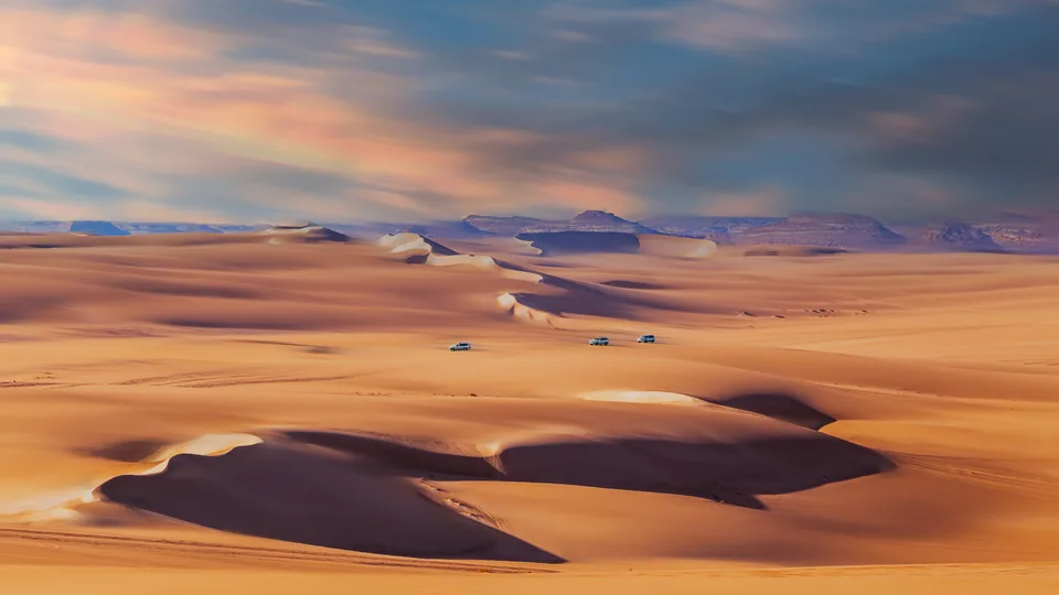 Four-wheel-drive safari vehicles among the golden dunes near Siwa.